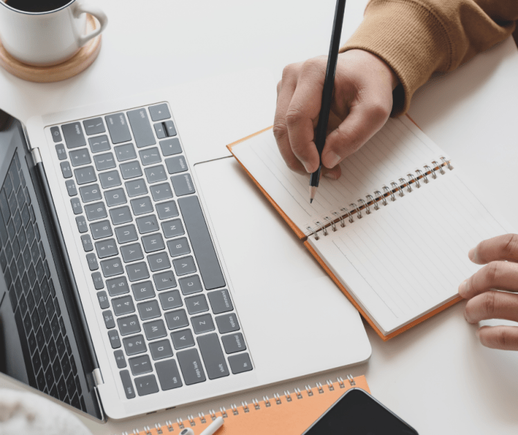 Laptop and someone writing in a notebook.