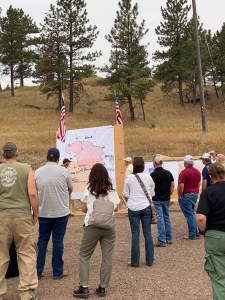 Picture of a crowd and Governor being briefed on a wildfire in front of a huge map of the fire.