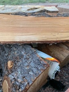 Split wood stacked for a campfire with burning paper under it.