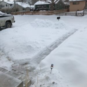 Snow covered lawn and road with a shoveled sidewalk.