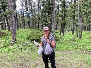 A woman holding two bags of morels while standing in a forest.