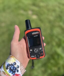 A hand is holding a DeLorme inReach Explorer. Green grass is blurred in the background.