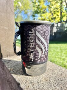 Jetboil camping stove sitting on a cement ledge with green grass in the background. 