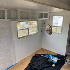 Picture of an RV with green painters tape around the window and one wall primed.