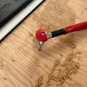 Picture of a paint scraper next to adhesive on an RV floor half scraped off.